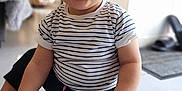 Kaël a rejoint le concours — aidez-le/la à gagner de superbes lots ! baby, barefoot, black_pants, bright, casual_clothing, child, closeup, curly_hair, cute, floor, happy, indoor, natural_light, person, portrait, sitting, smiling, striped_shirt, toddler, young_child