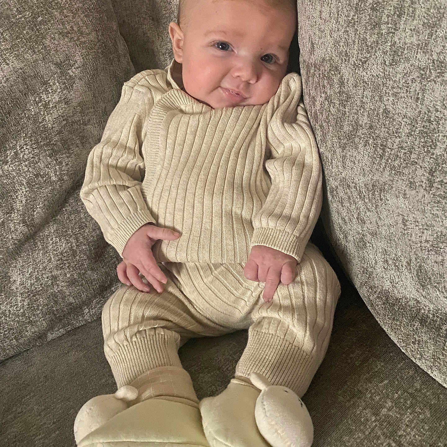 Ollie-Junior is registered to the contest to win money with this photo: apparel, baby, child, comfortable, couch, cozy, cute, cute_outfit, home, indoors, infant, knitwear, person, portrait, relaxing, seated, slippers, smile, soft, young