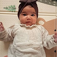 Soline participe au concours pour gagner de l'argent avec cette photo : baby, infant, headband, bow, white_outfit, play_mat, patterned_mat, lying_down, hands_raised, curious_expression, indoors, child, cute, smiling, face, person, portrait, soft_clothing, baby_girl, closeup