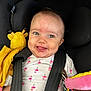baby, child, car_seat, toy, stuffed_animal, flamingo_pattern, onesie, face, smiling, tongue_out, seatbelt, infant, cute, happy, playful, colorful, plush_toy, sitting, indoors, person