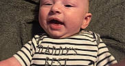 Sevyn is registered to the contest to win money with this photo: baby, infant, smiling, striped_shirt, text_on_clothing, blanket, lying_down, happy, cute, child, face, person, young_child, apparel, casual_wear, indoor, portrait, skin, head, expression