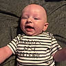 baby, infant, smiling, striped_shirt, text_on_clothing, blanket, lying_down, happy, cute, child, face, person, young_child, apparel, casual_wear, indoor, portrait, skin, head, expression