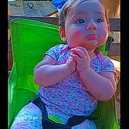Alice joined the competition — help win amazing prizes! toddler, child, baby, green_chair, clothing, patterned_pants, short_sleeve_shirt, hands_clasped, indoor, furniture, face, portrait, cute, expression, seatbelt, background_objects, wooden_table, colorful, casual, photography