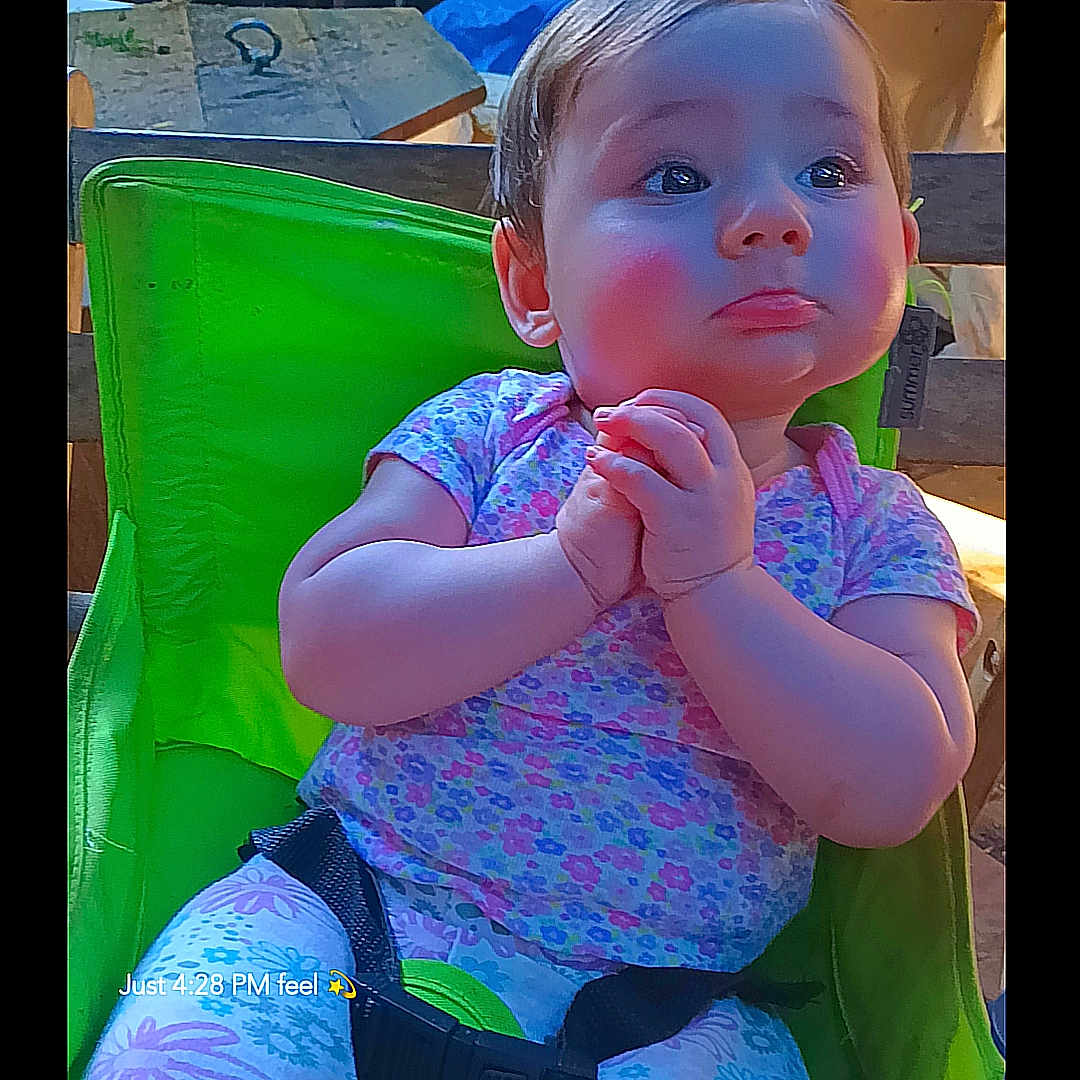 Alice joined the competition — help win amazing prizes! toddler, child, baby, green_chair, clothing, patterned_pants, short_sleeve_shirt, hands_clasped, indoor, furniture, face, portrait, cute, expression, seatbelt, background_objects, wooden_table, colorful, casual, photography