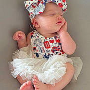 Barbara is registered to the contest to win money with this photo: baby, sleeping, infant, headband, bow, patterned_clothing, tulle_skirt, cute, peaceful, soft, newborn, hand_on_face, barefoot, pink_skin, resting, portrait, closeup, indoors, child, adorable