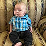 baby, child, infant, plaid_shirt, blue_shirt, black_pants, barefoot, sofa, upholstery, patterned_fabric, seated, indoor, person, cute, young, portrait, furniture, home, expression, serious