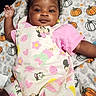 baby, infant, child, blanket, pumpkin, pattern, pink_clothing, cartoon_characters, cute, smiling, face, hand, curly_hair, lying_down, soft_texture, indoors, portrait, happy, toddler, playful