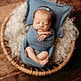 newborn, baby, swaddled, sleeping, basket, blue_wrap, headband, wooden_floor, fluffy_wool, peaceful, infant, portrait, cozy, cute, small_hands, tiny_feet, soft_texture, resting, indoors, warm_lighting