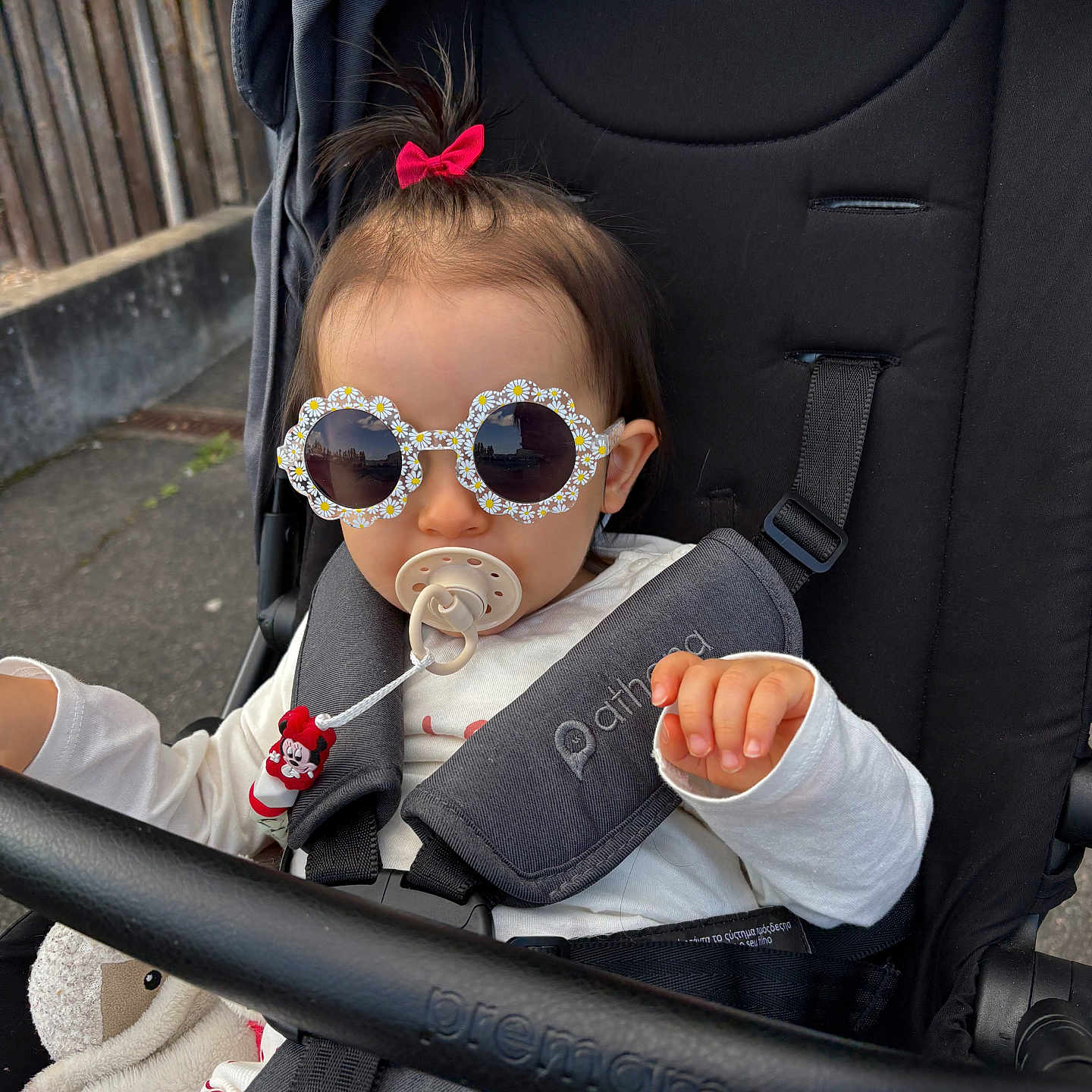 Kamélya participe au concours pour gagner de l'argent avec cette photo : toddler, child, sunglasses, pacifier, stroller, bow, hair, hand, clothing, white_shirt, baby_accessory, outdoor, seatbelt, black_stroller, cute, fashion, person, baby, walking, playful