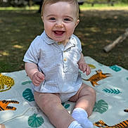 Theo is registered to the contest to win money with this photo: baby, child, smiling, outdoor, blanket, animal_print, grass, socks, shirt, happy, sitting, face, nature, cute, portrait, infant, sunlight, park, playful, young