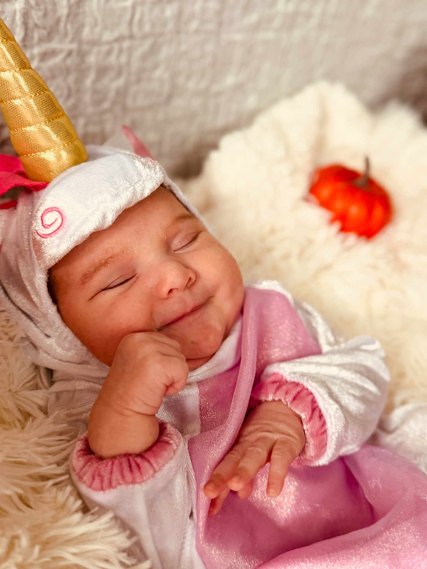 Sayda is registered to the contest to win money with this photo: baby, sleeping, unicorn_costume, costume, horn, pink_clothing, fluffy_blanket, pumpkin, orange, cute, infant, hand, soft_texture, cozy, portrait, indoors, child, smiling, closed_eyes, cute_outfit