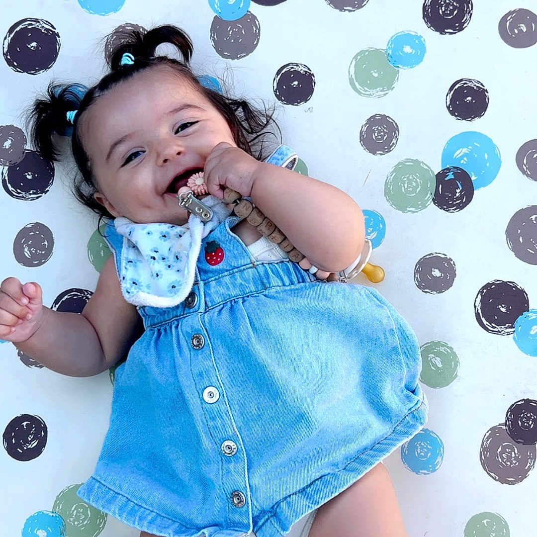 Andreïa participe au concours pour gagner de l'argent avec cette photo : accessory, baby, barefoot, beads, blue_dress, buttoned_dress, chewing, child, cute, grass, happy, infant, lying_down, outdoor, pigtails, playmat, polka_dot, smiling, toy, white_bib