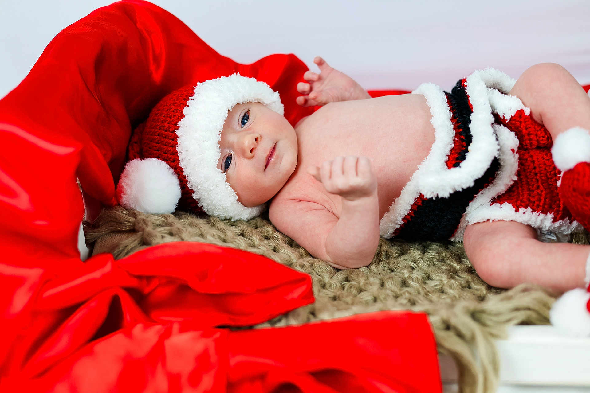Kagen is registered to the contest to win money with this photo: baby, infant, santa_hat, knitted_clothing, red_fabric, blanket, cute, holiday, christmas, festive, lying_down, indoors, portrait, soft_texture, warm_colors, child, face, smiling, newborn, cozy