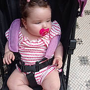 Alyannah participe au concours pour gagner de l'argent avec cette photo : baby, pacifier, stroller, child, infant, pink, patterned_clothing, toddler, seatbelt, hair_ties, curly_hair, indoor, floor_tiles, plump_legs, cute, small_hands, looking_away, sitting, casual, comfort