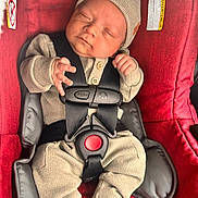 Adrian is registered to the contest to win money with this photo: baby, infant, car_seat, red, beige_clothing, knit_hat, knit_outfit, sleeping, straps, safety_harness, child, newborn, cute, small_hands, white_socks, indoor, closeup, peaceful, portrait, soft_lighting