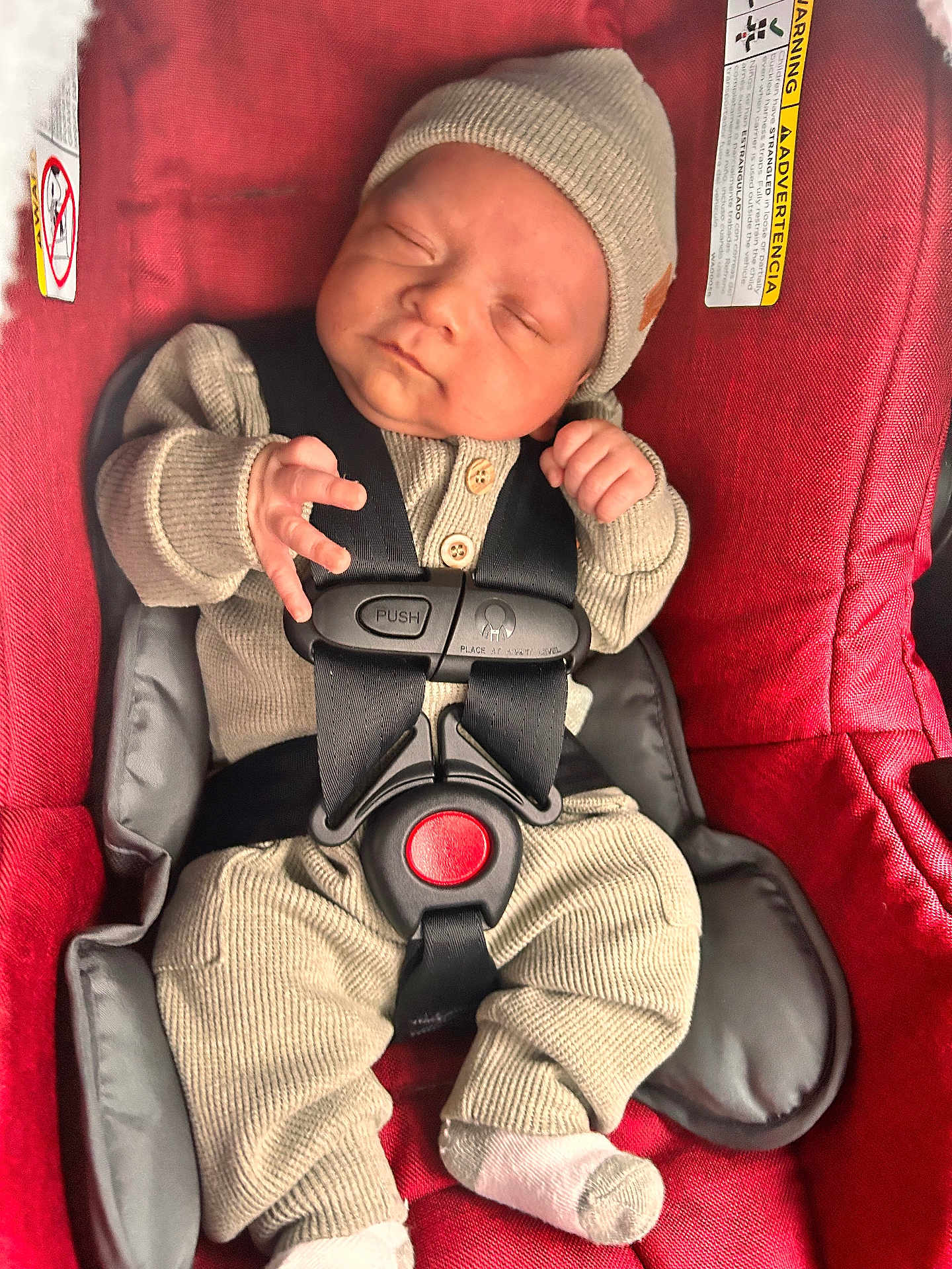 Adrian is registered to the contest to win money with this photo: baby, infant, car_seat, red, beige_clothing, knit_hat, knit_outfit, sleeping, straps, safety_harness, child, newborn, cute, small_hands, white_socks, indoor, closeup, peaceful, portrait, soft_lighting