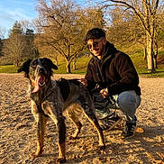 Seiko participe au concours pour gagner de l'argent avec cette photo : dog, man, sunglasses, sand, trees, blue_sky, sunlight, park, outdoor, smiling, pet, leash, casual_clothing, happy, nature, shadow, grass, walking_shoes, tree_branches, daytime