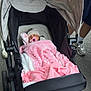 baby, blanket, stroller, pacifier, hat, sleeping, person, footwear, shoe, sock, outdoor, pavement, clothing, hand, wheel, fabric, infant, resting, parent, transport