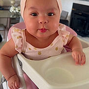 Yarely is registered to the contest to win money with this photo: baby, infant, high_chair, headband, pink_clothing, tongue_out, cute, big_eyes, chubby_cheeks, smiling, hands, face, eyes, dining_room, mirror, decor, wall_art, home_interior, tray, seat