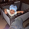 baby, child, playpen, hat, blue_hat, smile, indoor, carpet, person, jeans, furniture, home, baby_clothes, hand, face, happy, toy, parent, room, floor