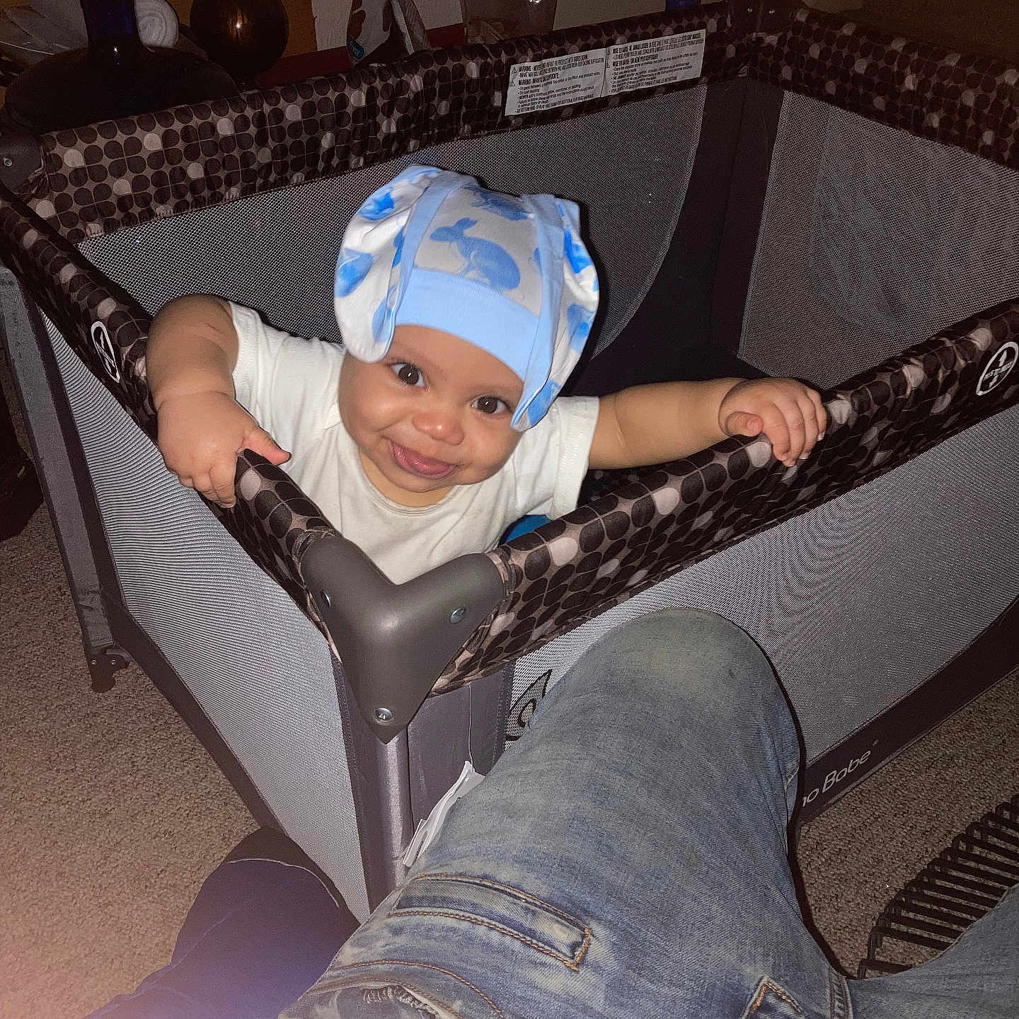 Aiko is registered to the contest to win money with this photo: baby, child, playpen, hat, blue_hat, smile, indoor, carpet, person, jeans, furniture, home, baby_clothes, hand, face, happy, toy, parent, room, floor