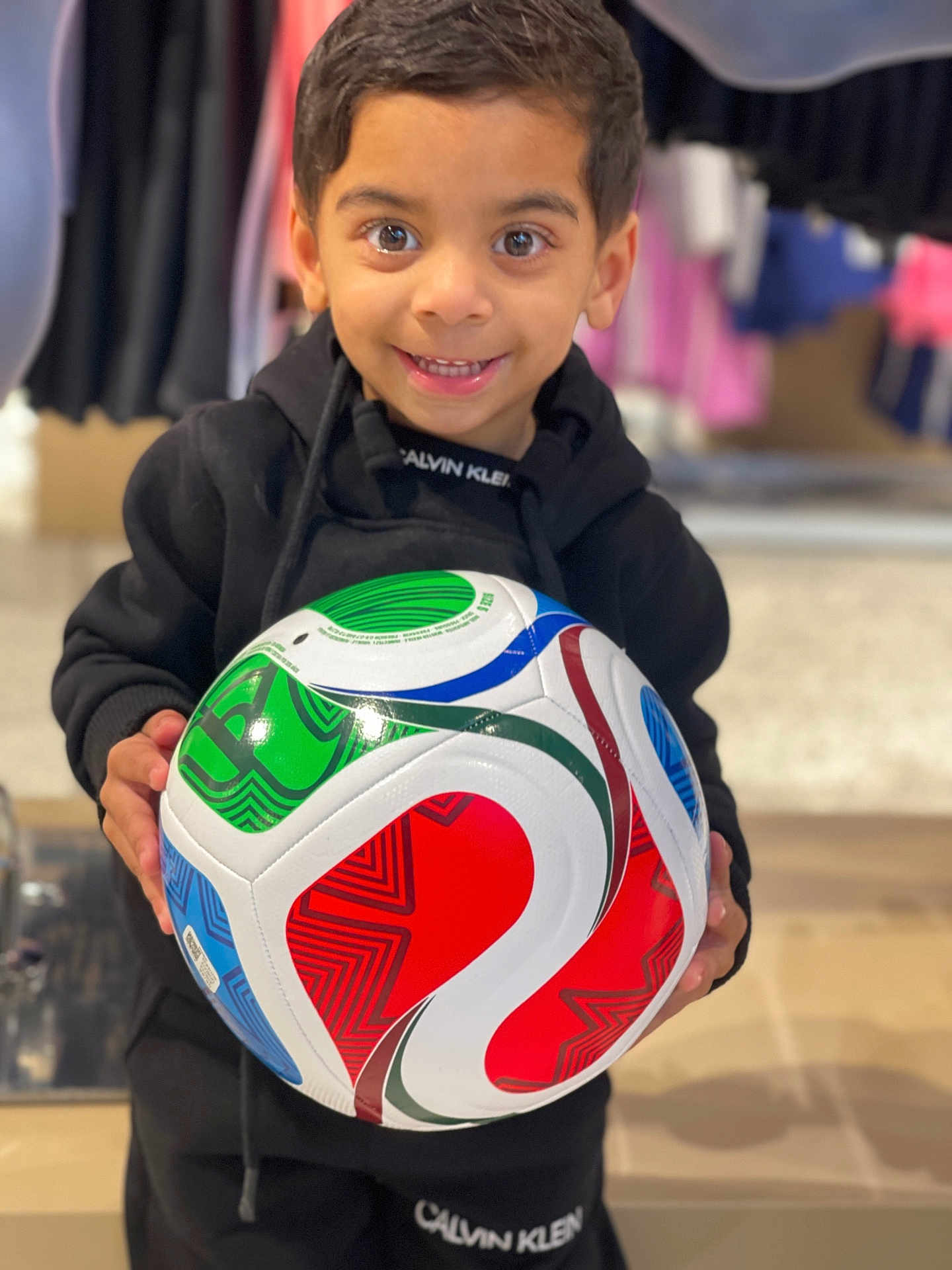 Ishan joined the competition — help win amazing prizes! child, boy, soccer_ball, black_clothing, smiling, indoor, calvin_klein, holding, happy, bright, colorful, sport, portrait, casual, young, person, apparel, face, eyes, hands