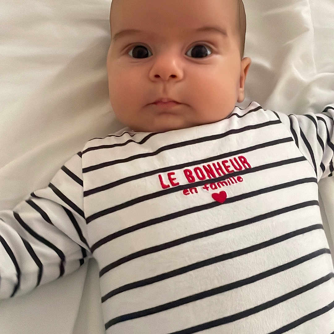 Yassine a rejoint le concours — aidez-le/la à gagner de superbes lots ! baby, bed, black_and_white, child, curious, cute, expression, eyes, face, indoors, infant, lying_down, newborn, portrait, red_text, sleepwear, soft_lighting, striped_clothing, text_on_clothing, white_bed