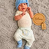 baby, infant, child, newborn, portrait, lying_down, smiling, blue_hat, pom_pom, onesie, elephant, striped_pants, socks, fluffy_rug, wooden_sign, milestone, one_month, indoors, cozy, family_photo
