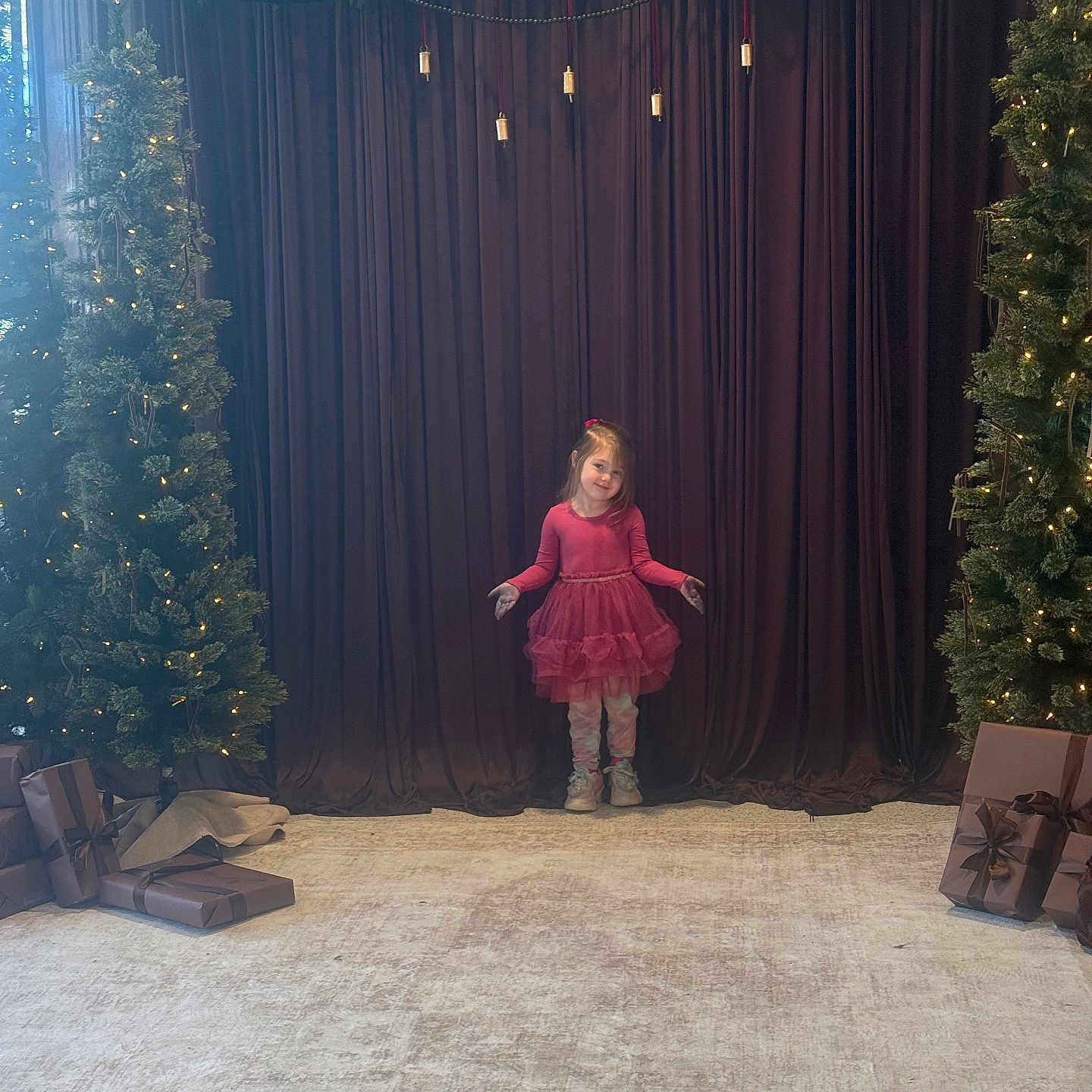 Althea is registered to the contest to win money with this photo: carpet, celebration, child, christmas_tree, curtain, decorations, event, festive, gift_wrap, girl, happy, holiday_decor, indoor, lights, pink_dress, pose, presents, smile, stage, young
