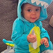 Kayden joined the competition — help win amazing prizes! baby, blanket, blue_clothing, child, costume, couch, cozy, cute, dinosaur_onesie, eyes, face, hand, home, hood, indoor, person, plush, seated, smiling, toddler