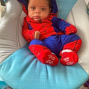 Kayden is registered to the contest to win money with this photo: baby, infant, spiderman_costume, costume, blue_cushion, red, blue, baby_clothing, child, face, cute, indoor, seated, looking_at_camera, expression, small_hands, footwear, hood, baby_boy, portrait