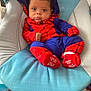 baby, infant, spiderman_costume, costume, blue_cushion, red, blue, baby_clothing, child, face, cute, indoor, seated, looking_at_camera, expression, small_hands, footwear, hood, baby_boy, portrait