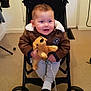 toddler, child, stroller, plush_toy, dog_toy, jacket, pacifier, indoor, carpet, door, keys, person, clothing, wheel, baby, cute, seated, face, happy, hand