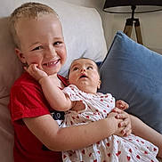 Simon a rejoint le concours — aidez-le/la à gagner de superbes lots ! child, baby, smiling, couch, pillow, lamp, red_shirt, white_dress, hearts_pattern, indoor, brother, sibling, happy, holding, cute, family, portrait, home, seated, love