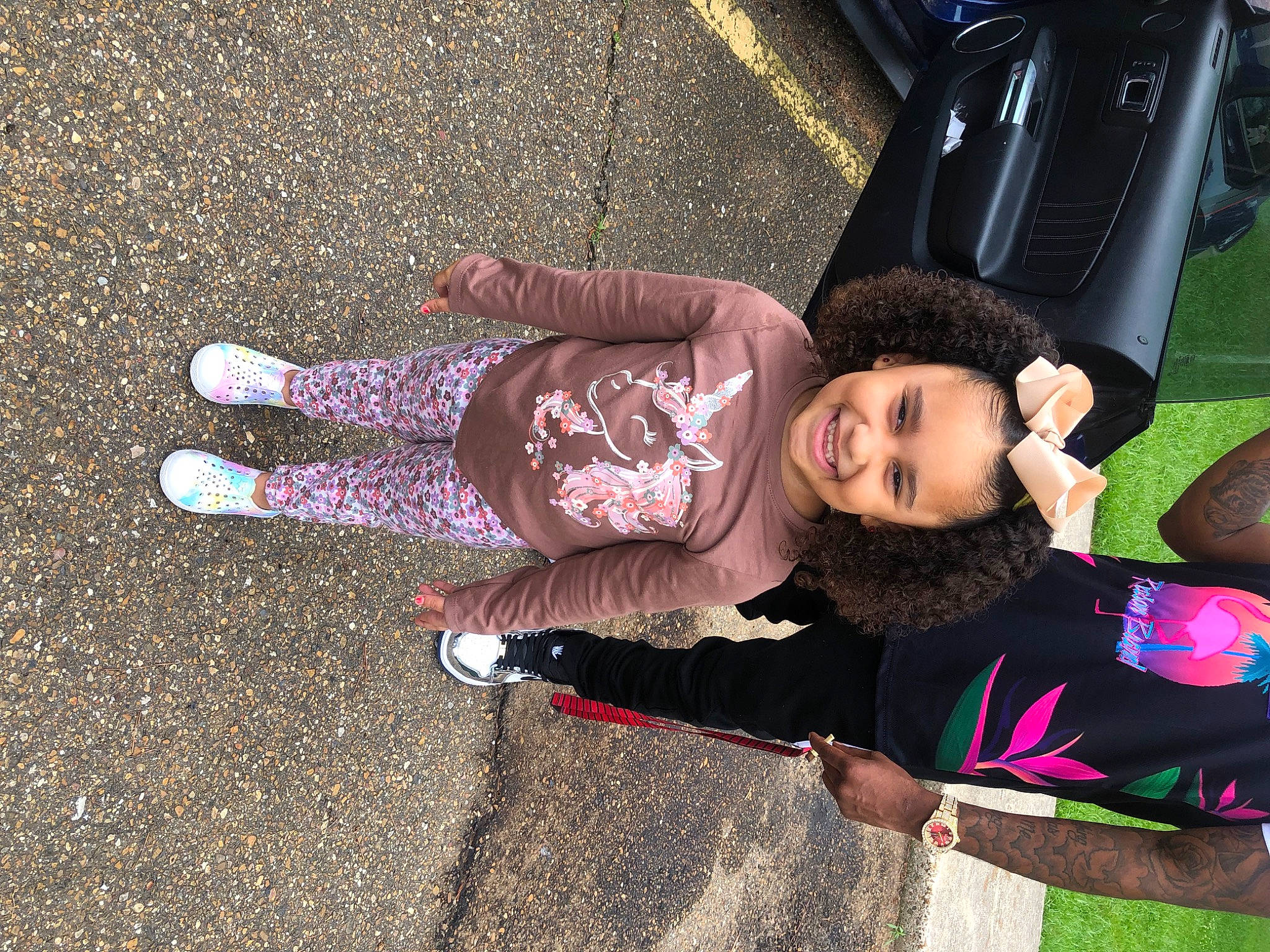 Ariah is registered to the contest to win money with this photo: asphalt, automotive_exterior, automotive_lighting, automotive_tire, child, finger, fun, grass, hand, happy, headwear, human_leg, joy, leisure, motor_vehicle, person, public_space, road_surface, sneakers, tire