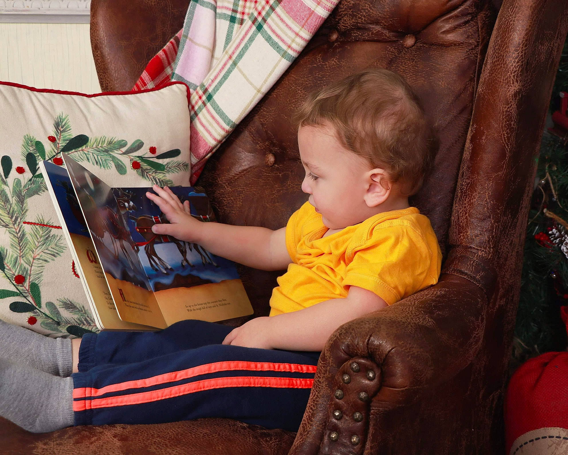 Gannon is registered to the contest to win money with this photo: baby, child, christmas, christmas_eve, holiday, lap, person, play, reading, room, sitting, toddler