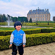 Markus participe au concours pour gagner de l'argent avec cette photo : black_pants, blue_jacket, boy, casual_wear, chateau, child, cloudy_sky, daytime, fountain, garden, grass, hedges, historic_building, outdoor, pathway, portrait, smiling, sneakers, standing, young