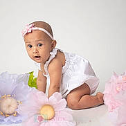 Maria Luiza is registered to the contest to win money with this photo: baby, child, crawling, white_dress, headband, pink_flower, large_flowers, pastel_colors, curious_expression, studio_photo, indoor, portrait, cute, infant, flower_decoration, soft_lighting, white_background, kneeling, young_child, adorable
