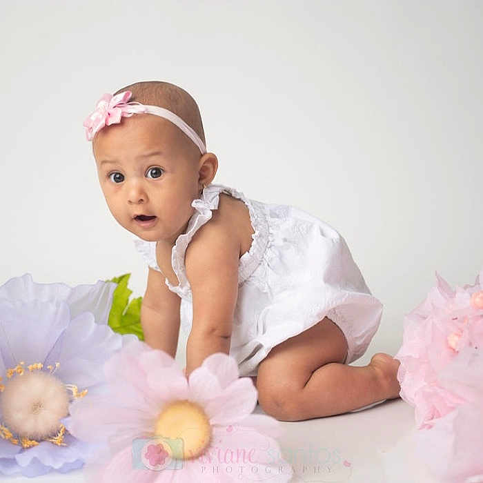 Maria Luiza is registered to the contest to win money with this photo: adorable, baby, child, crawling, curious_expression, cute, flower_decoration, headband, indoor, infant, kneeling, large_flowers, pastel_colors, pink_flower, portrait, soft_lighting, studio_photo, white_background, white_dress, young_child