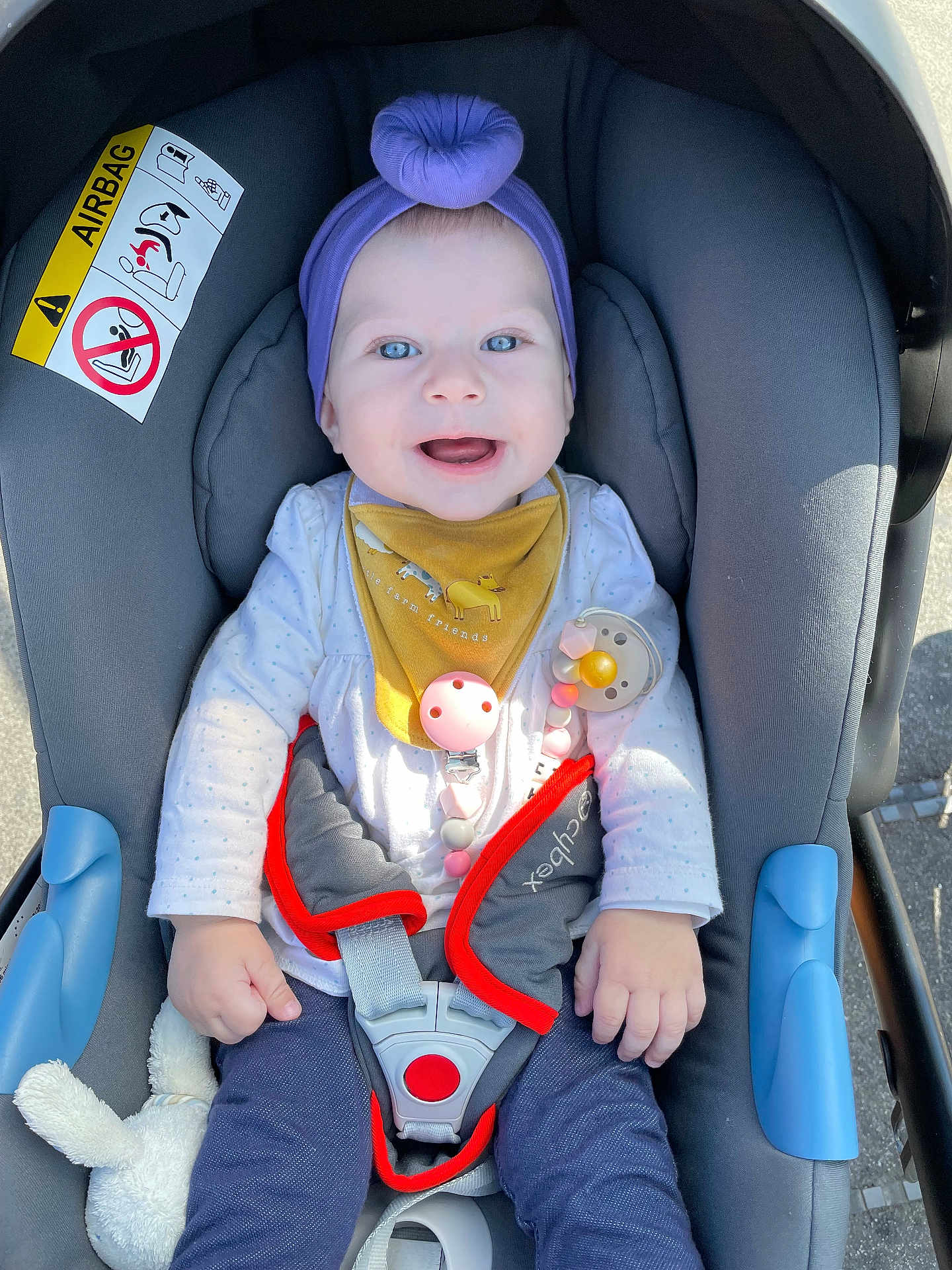 Ruth joined the competition — help win amazing prizes! baby, child, car_seat, purple_headband, pacifier_clip, smiling, blue_eyes, white_shirt, yellow_bib, gray_cushion, safety_harness, toy, outdoor, daylight, infant, cute, happy, casual_clothing, toddler, seatbelt