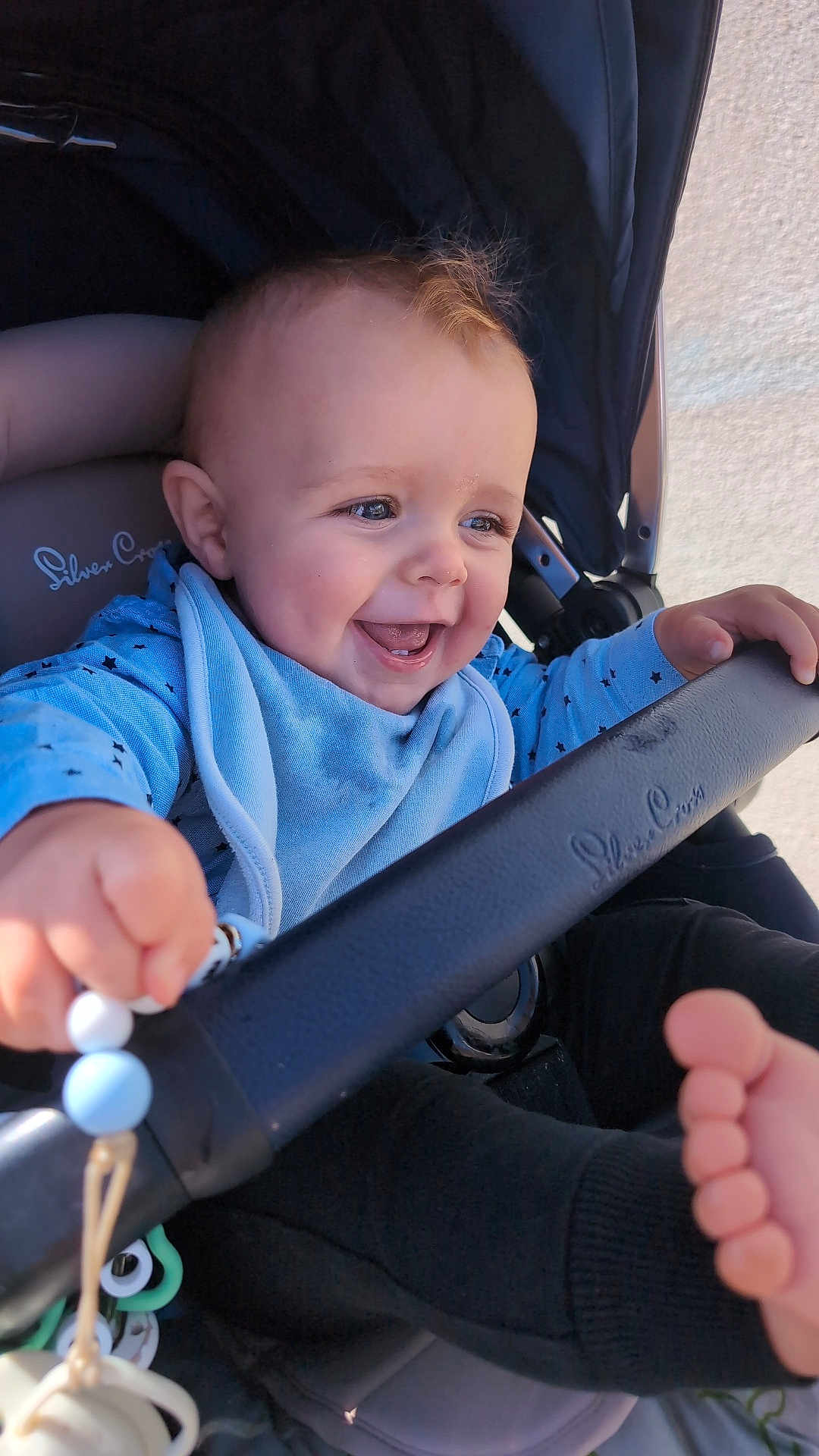 Freddie is registered to the contest to win money with this photo: baby, child, stroller, blue_clothing, bib, hand, foot, pacifier, smiling, happy, infant, closeup, cute, toy, seat, grip, outdoor, daylight, face, expression