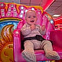 Freddie is registered to the contest to win money with this photo: baby, child, amusement_ride, pink_seat, smiling, happy, indoor, colorful, lights, sun_design, knit_clothing, seatbelt, playful, entertainment, fun, portrait, cute, infant, joy, leisure