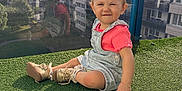 Lyna participe au concours pour gagner de l'argent avec cette photo : toddler, child, sitting, overalls, pink_shirt, shoes, outdoor, balcony, glass_railing, reflection, urban, buildings, sky, clouds, grass, daylight, portrait, cute, playful, sunlight