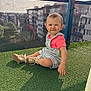 toddler, child, sitting, overalls, pink_shirt, shoes, outdoor, balcony, glass_railing, reflection, urban, buildings, sky, clouds, grass, daylight, portrait, cute, playful, sunlight