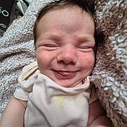 Alexander is registered to the contest to win money with this photo: baby, smile, tongue_out, blanket, onesie, infant, close_up, soft_texture, cute, happy, sleepy, child, newborn, cozy, indoor, face, expression, skin, head, comfort