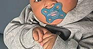 Cassius is registered to the contest to win money with this photo: baby, pacifier, hoodie, grey_clothing, infant, cute, hands, portrait, face, young_child, indoors, soft_lighting, expression, comfortable, casual, sitting, child, looking_at_camera, skin, head