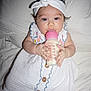 baby, child, bottle, feeding, headband, white_clothing, embroidery, bed, blanket, infant, cute, portrait, lying_down, hand, feet, person, indoors, soft_lighting, smile, milk