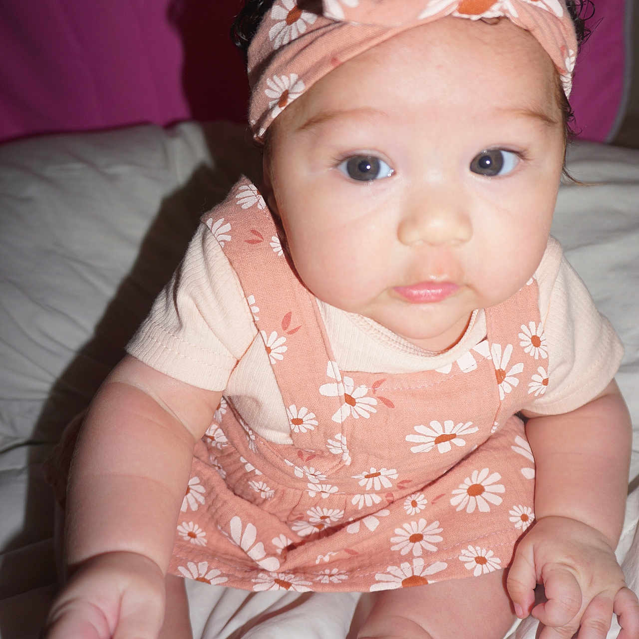 Aya is registered to the contest to win money with this photo: baby, bed, blanket, child, chubby, curly_hair, cute, dress, expression, face, feet, floral_pattern, hands, headband, indoors, infant, pink, portrait, sitting, skin