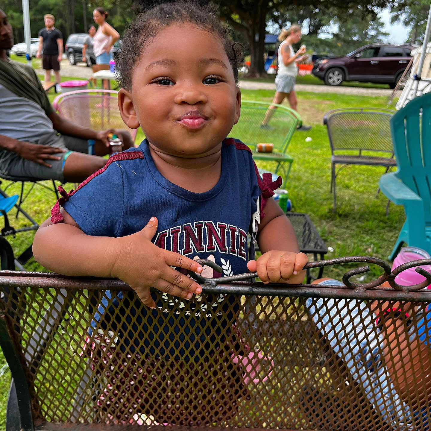 Lolani Davenport is registered to the contest to win money with this photo: blue_shirt, car, casual_clothing, child, curly_hair, daytime, event, fence, fun, grass, hand, metal_chair, outdoor, park, people, person, playful, smile, toddler, tree