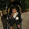 baby, child, clothing, curious, food, greenery, ice_cream, night, outdoor, pavement, person, shoes, sidewalk, sitting, snack, stroller, toddler, tree, urban, young_child